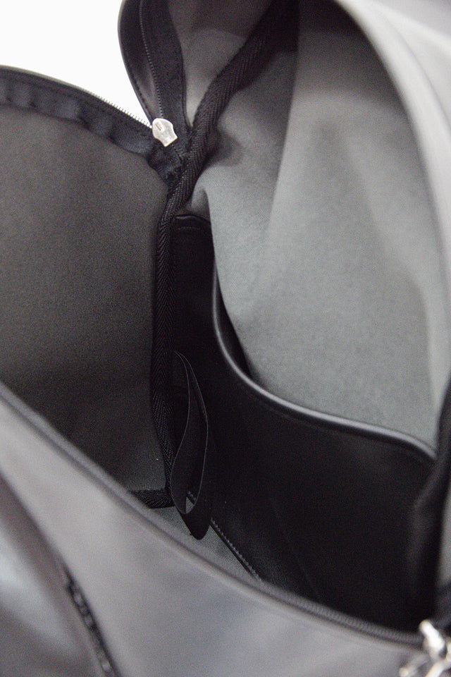 Zoom sur l'intérieur du sac à dos mono bandouliere noir pratique et intemporel en cuir vegan de raisin, made in france, le Pilot Bag. On aperçoit à l'intérieur une poche ordinateur en cuir vegan de raisin et un elastique sur le côté droit du sac.