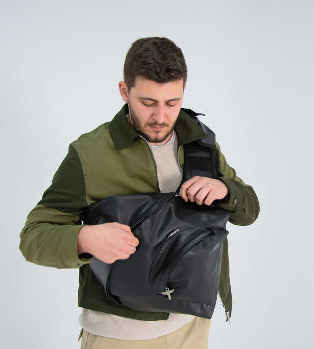 Un homme de dos avec une veste color block verte, porte le sac à dos made in France vegan Pilot Bag. Le 1er sac à dos made in france en raisin au design issu des années 90. Il le fait pivoter autour de son buste, pour un accès pratique et sécurisé à toutes les poches.