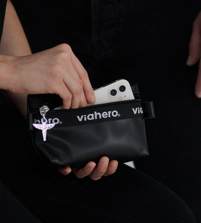 Zoom sur une main féminine qui glisse un iphone dans la pochette zippée tendance et urbaine noir, en cuir vegan de raisin made in france. 