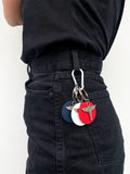 Photo mode femme urbaine. Une silhouette en jean noir de profil avec attaché à la ceinture trois porte clés personnalisable en métal argent et rond de cuir vegan en raisin bleu, blanc et rouge, fabriqués en France. Un look vintage qui rappelle les années 90.